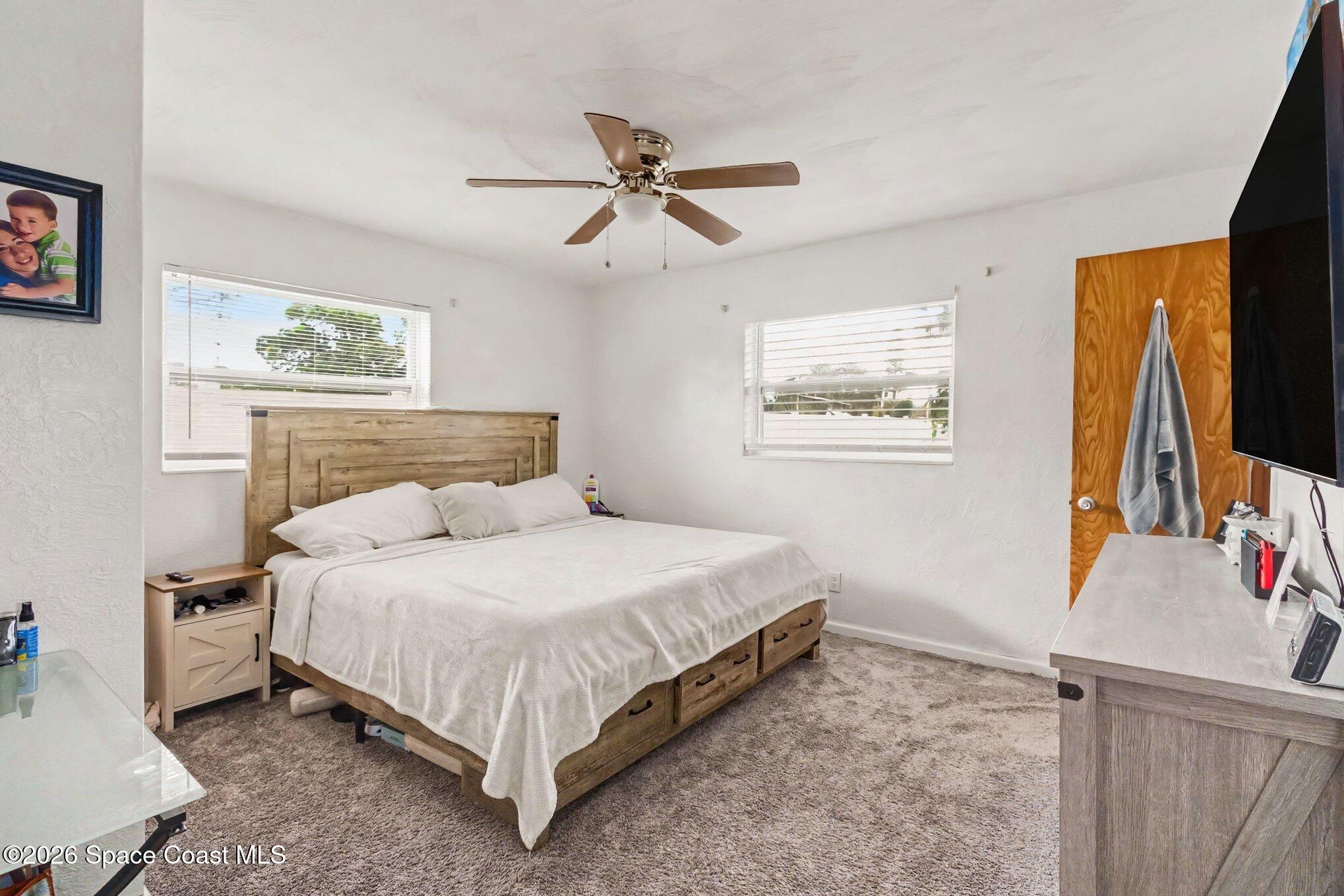 Bedroom with a wooden storage bed, white bedding, carpet, and a ceiling fan.