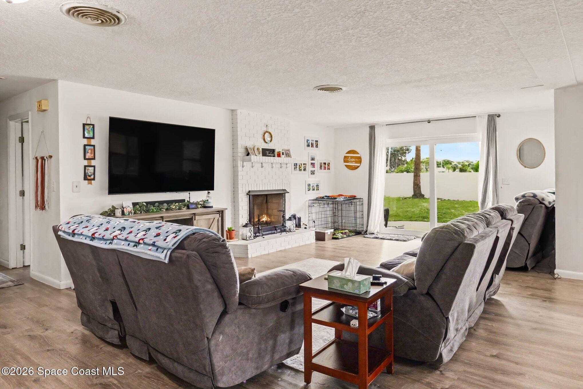Living room with gray sectional sofas, a white brick fireplace, and sliding doors to the backyard.