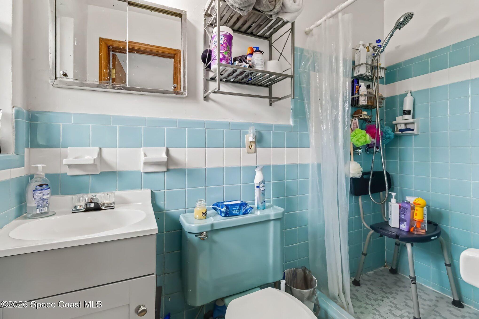 Bathroom with turquoise-and-white tile, a white vanity, and a shower behind a translucent curtain.