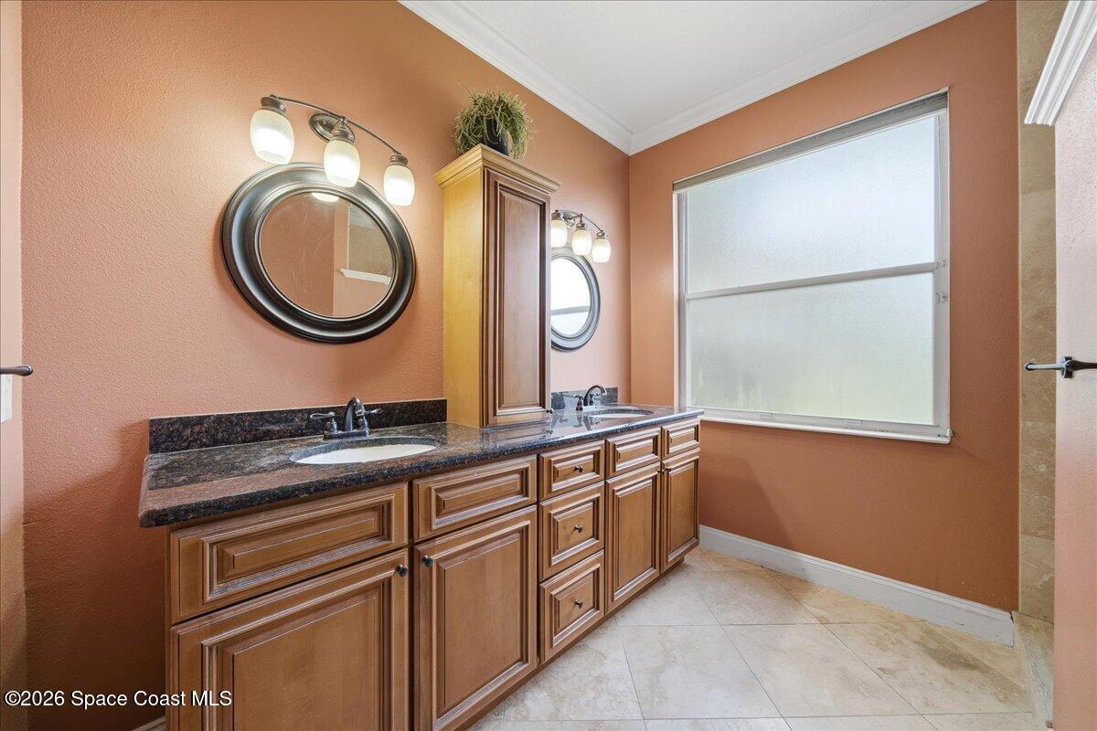 Bathroom with a double-sink wood vanity, dark stone counters, round mirrors, and a large window.