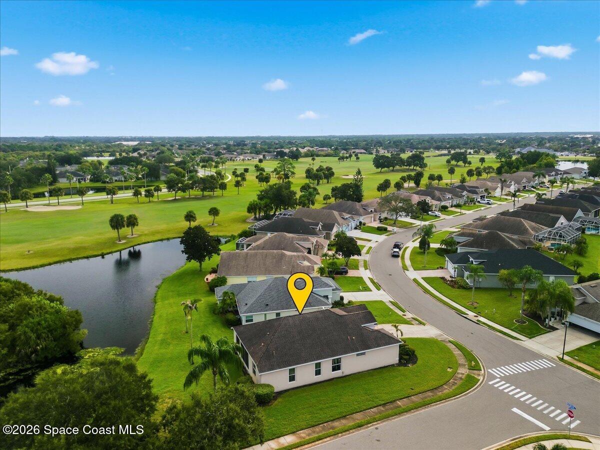 Aerial view of the home beside a pond, with a golf course and neighborhood beyond.