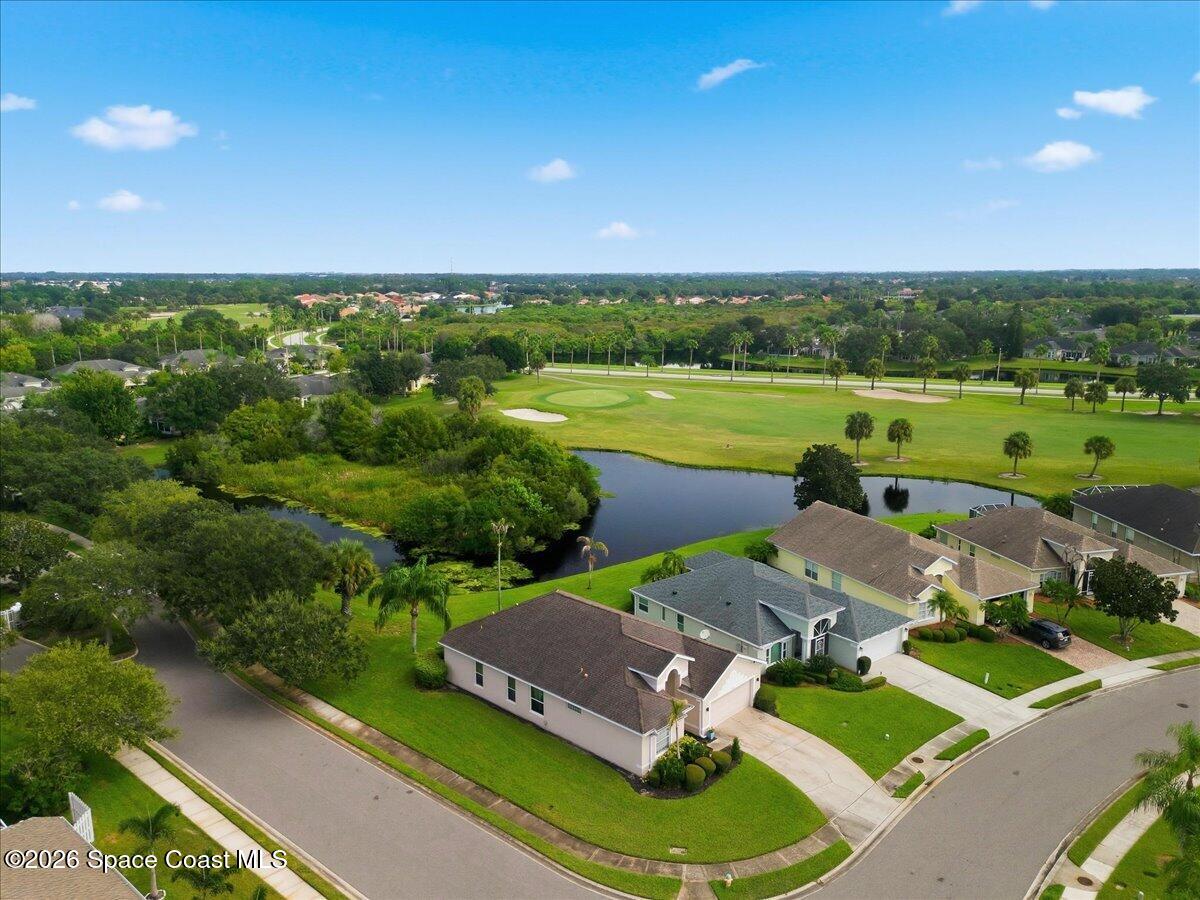 Aerial view of homes beside a golf course and pond, with fairways and sand bunkers.