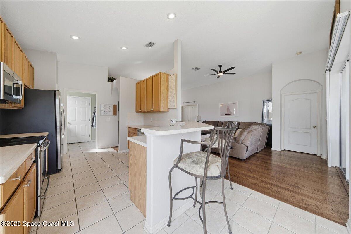 Open kitchen with a white breakfast bar and stools adjoining a furnished living room.