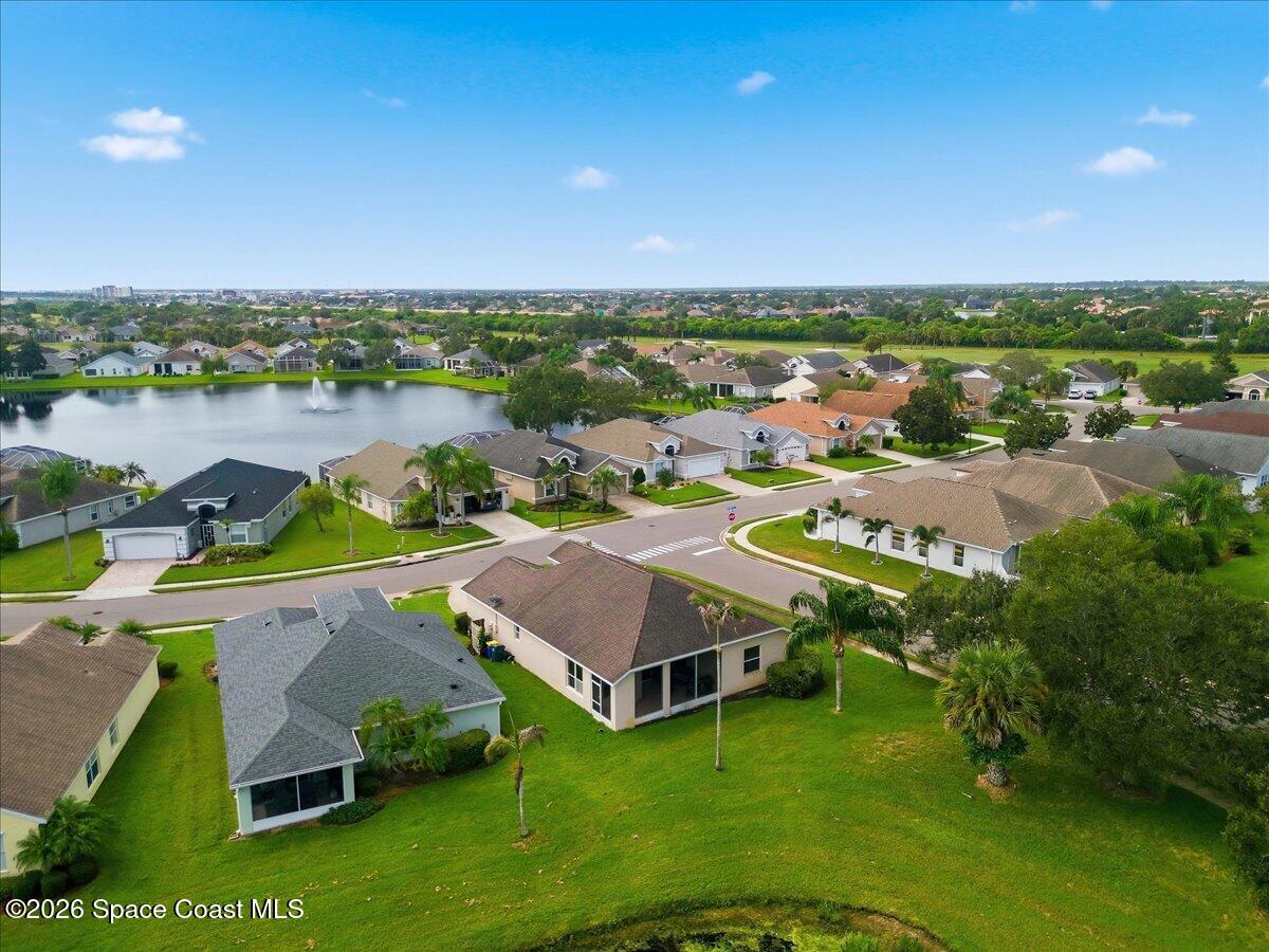 Aerial view of a home with a broad green backyard, neighboring houses, and a fountain pond.