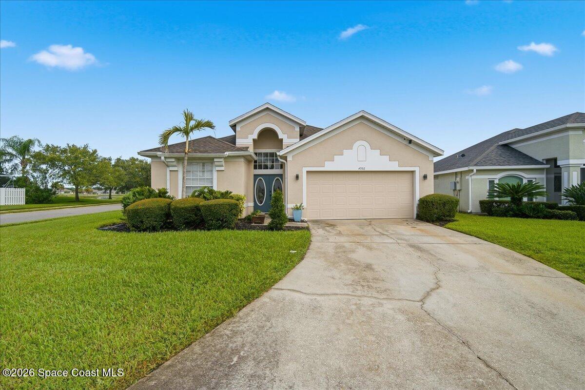 Beige stucco home with an arched entry, two-car garage, palm tree, and broad driveway.