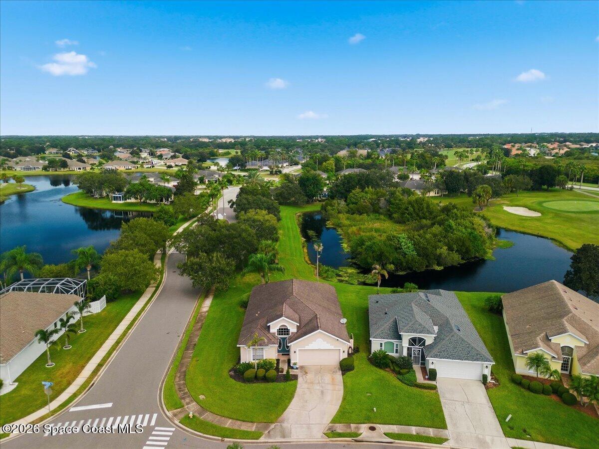 Aerial view of a home with a curved driveway, beside ponds and a golf course.