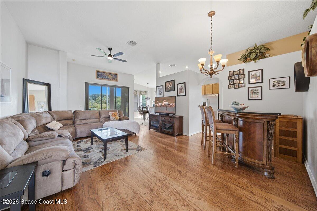 Open-plan living and dining room with hardwood floors, a sectional sofa, and a wood bar with stools.