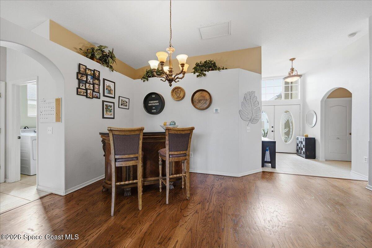 Dining area with a counter-height table, two chairs, chandelier, and hardwood floors.