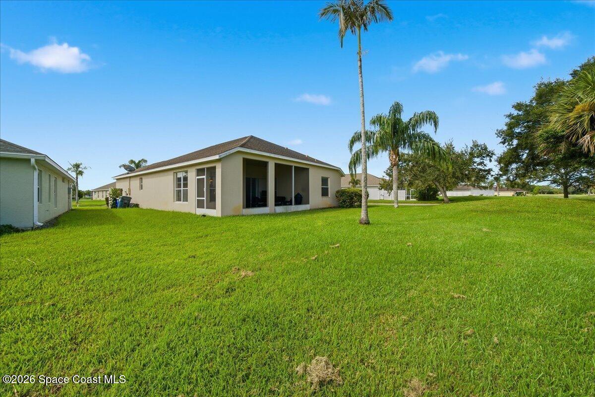 Single-story home with a covered rear patio, expansive lawn, and palm trees.
