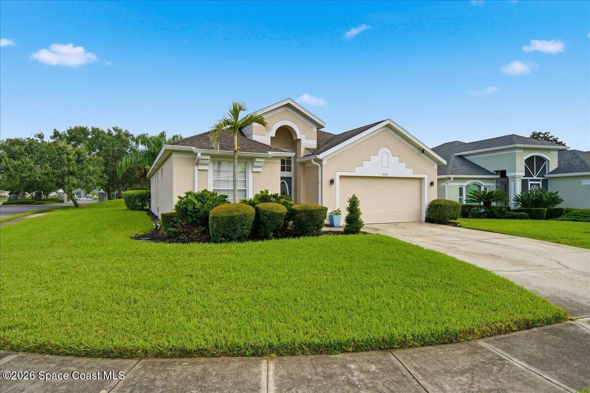 Beige stucco home with an arched entry, double garage, palm tree, and manicured front lawn.