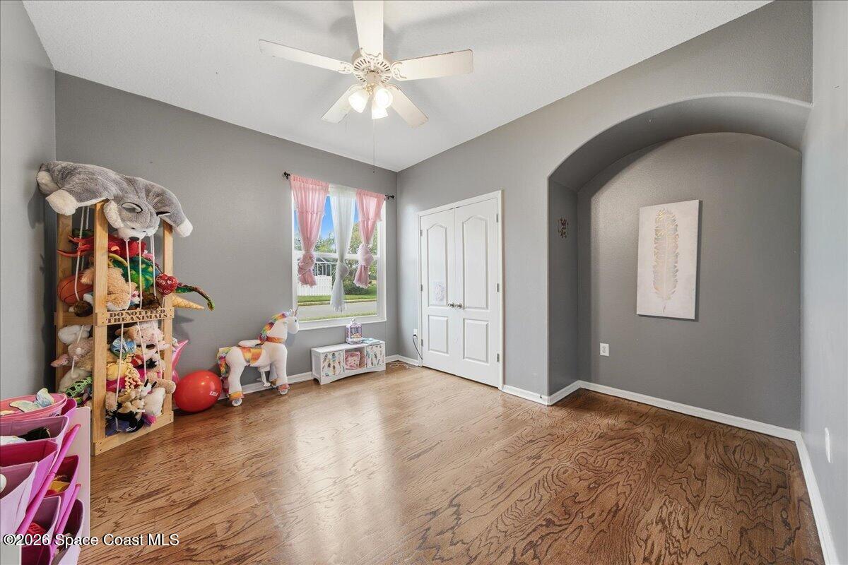 Bedroom or playroom with hardwood floors, pink curtains, toy shelves, and an arched wall alcove.