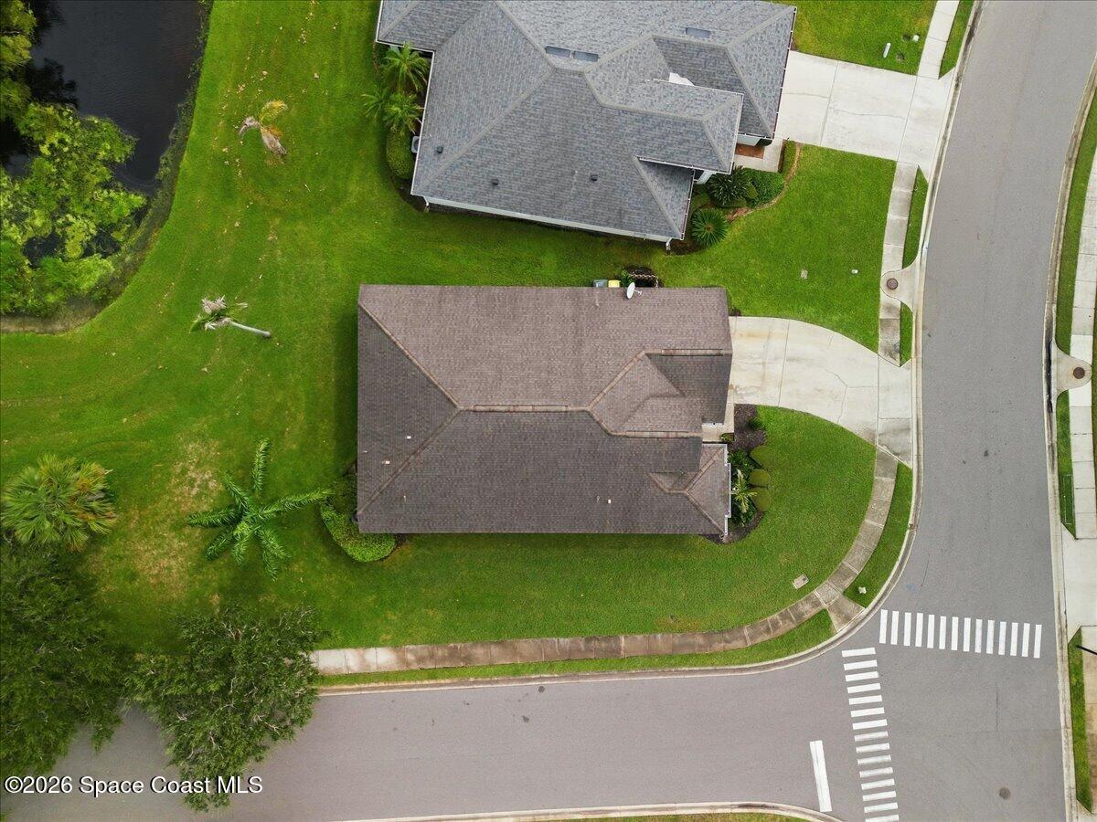 Aerial view of a corner-lot home with a broad lawn, nearby pond, and street intersection.