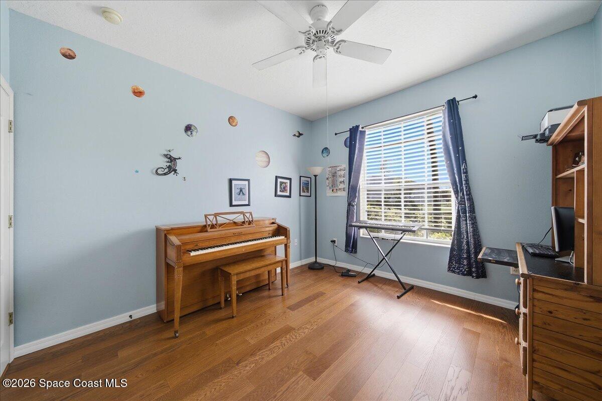 Furnished music room with an upright piano, keyboard, hardwood floors, and space-themed decorations.