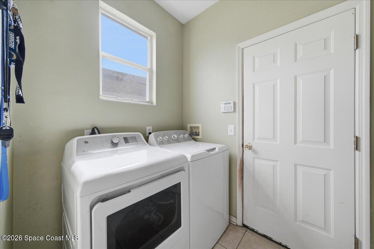 Laundry room with a front-loading dryer, top-loading washer, and window.