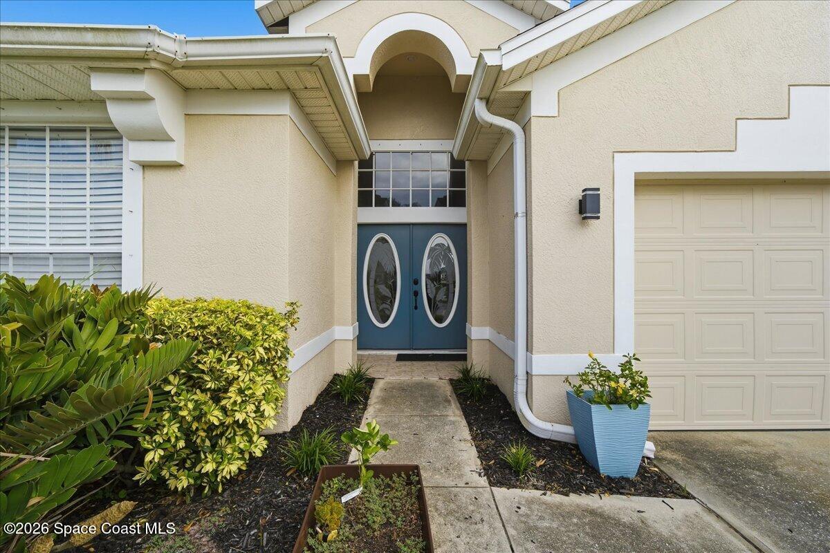 Cream stucco home with an arched entry, blue double doors, attached garage, and landscaped walkway.