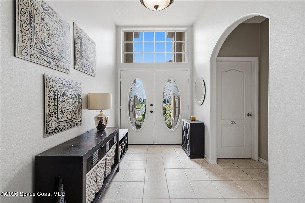 Entry foyer with oval-glass double doors, a transom window, tiled floors, and dark console tables.