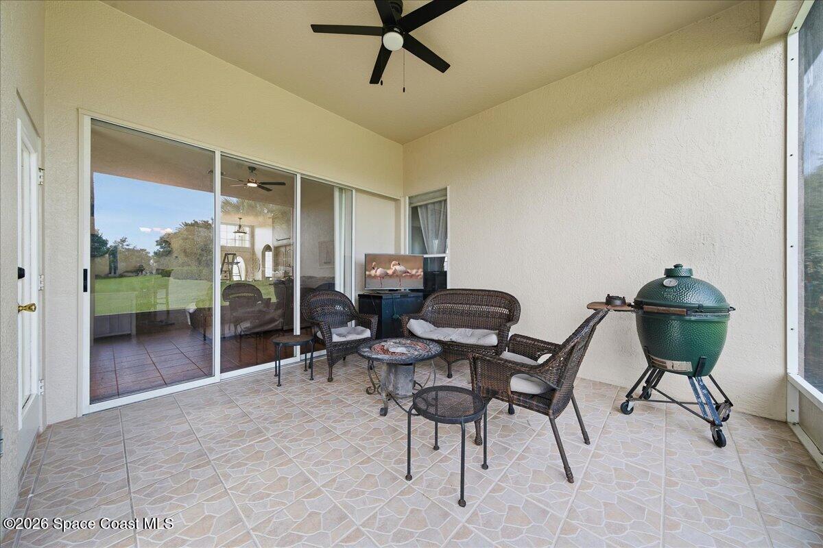 Covered patio with wicker seating and a green ceramic grill beside sliding glass doors.