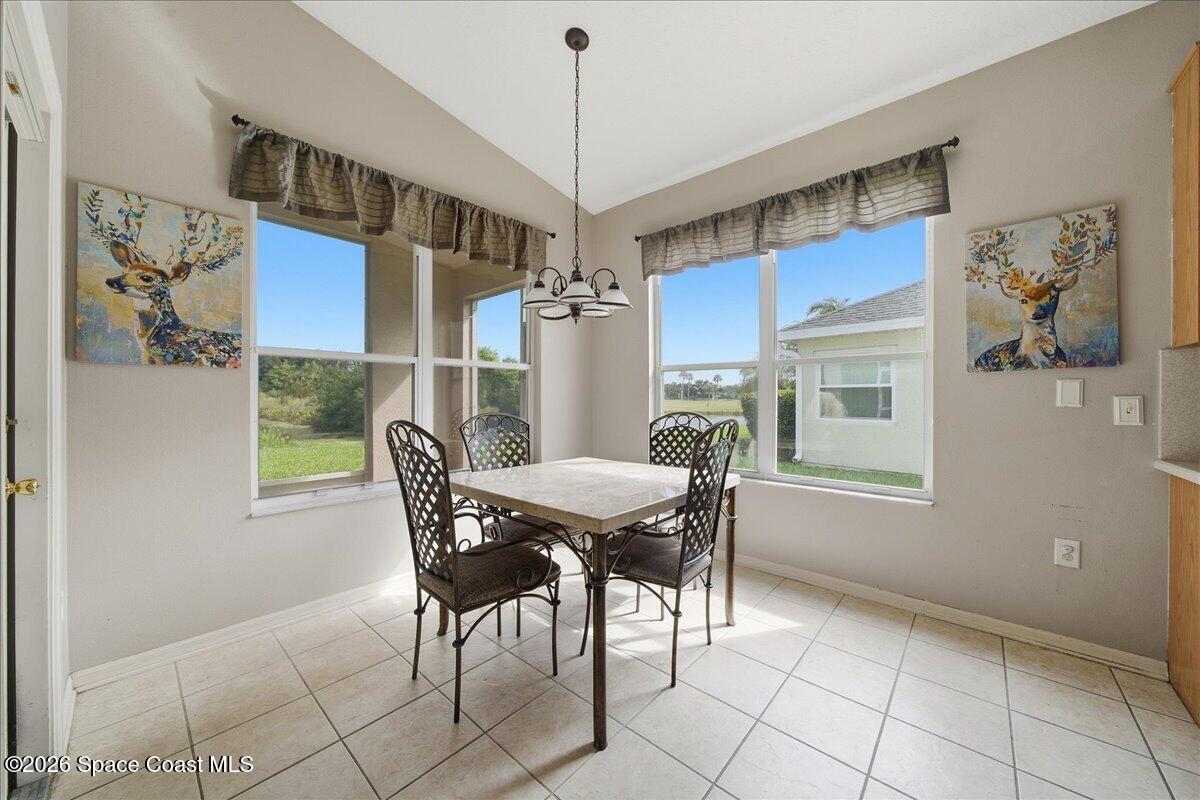 Dining nook with a square table and four chairs beside large windows overlooking a green yard.