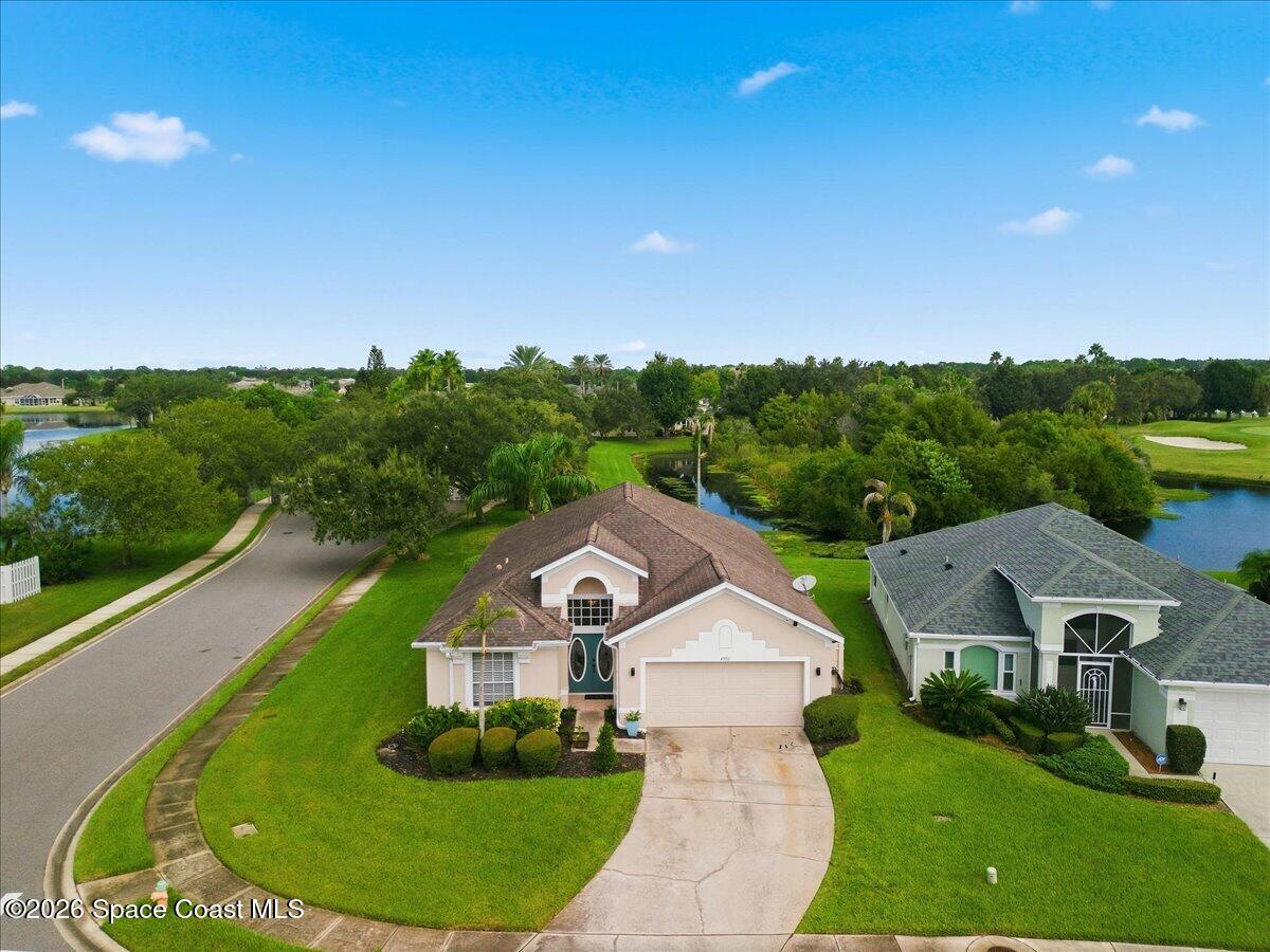 Aerial view of a home with a curved driveway, waterway, and golf course behind it.
