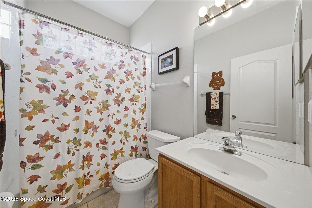Bathroom with leaf-patterned shower curtain, wood vanity, and large mirror.