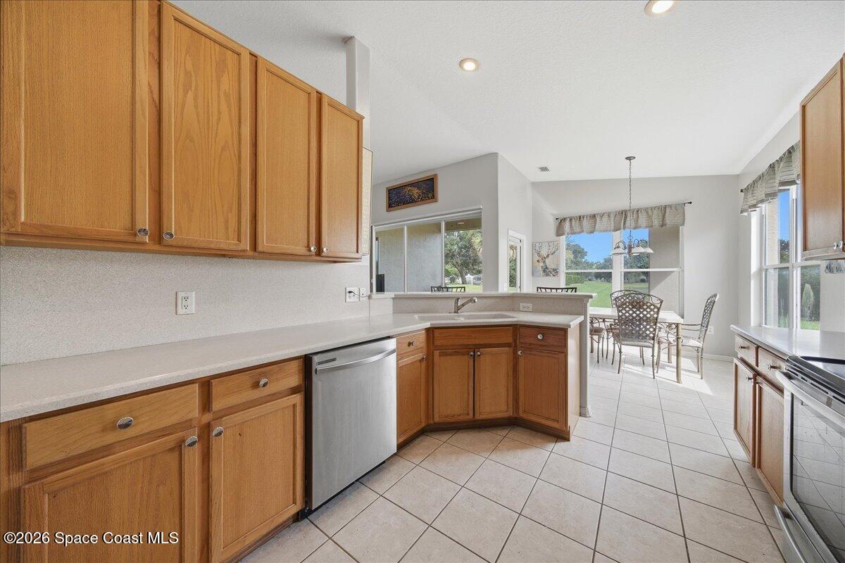 Kitchen with honey-toned wood cabinets, a peninsula sink, and a dining area beside large windows.