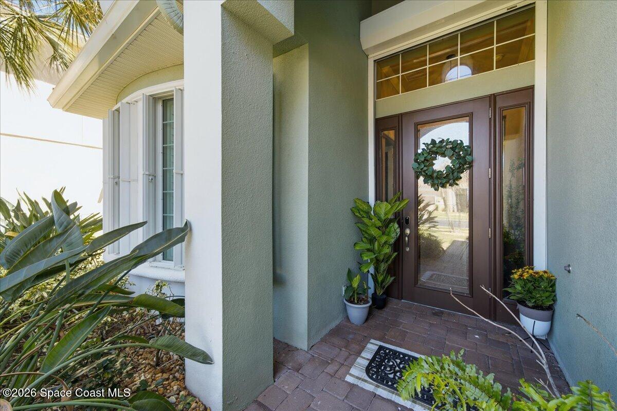 Front entrance with dark wood door, transom window, potted plants, and brick porch.