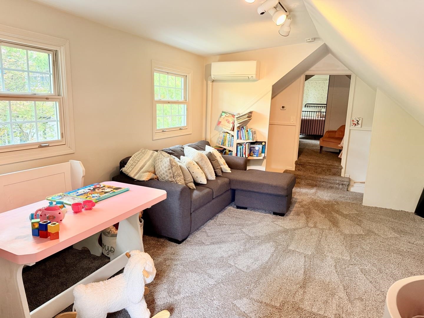 Upstairs playroom with a gray sectional, children’s toys, carpet, and sloped ceiling.