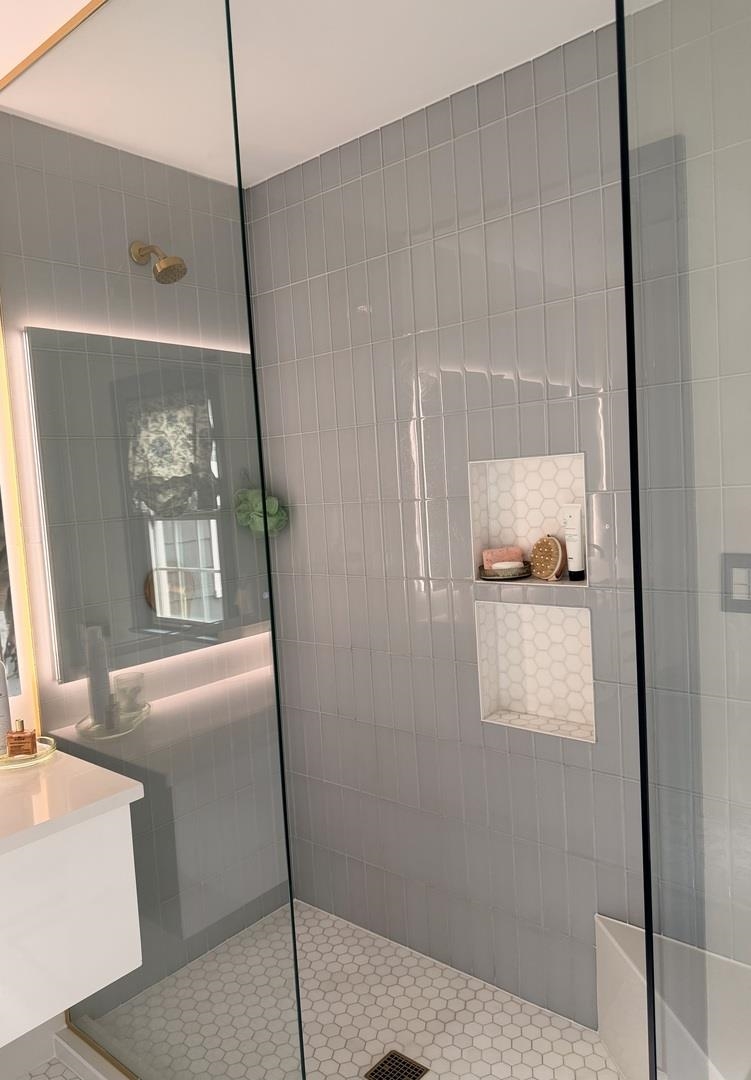 Walk-in shower with glass panels, tiled niches, a white hex tile floor, and brass fixtures.
