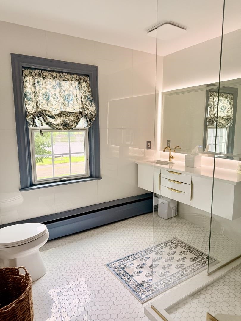 Bathroom with glass shower, brass vanity fixtures, hexagonal tile floor, and floral window shade.