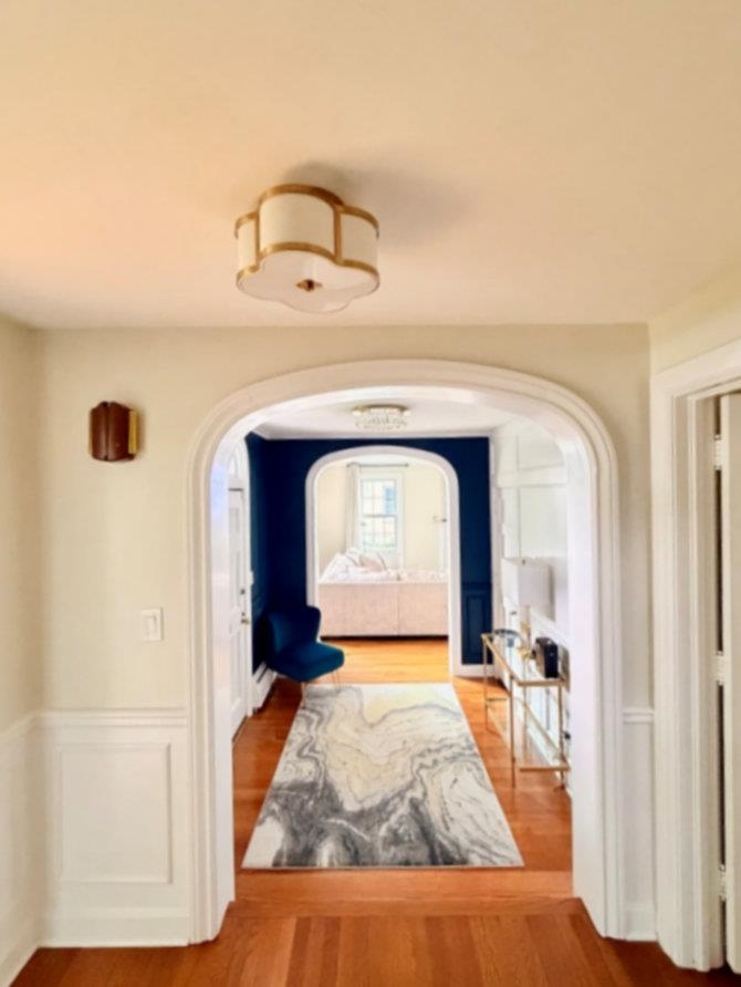 Furnished hallway with arched doorways, hardwood floors, and a patterned runner.