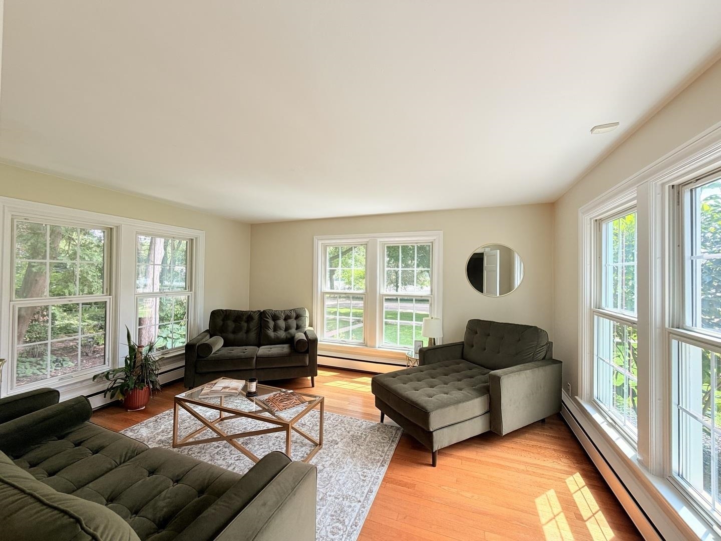 Living room with dark sofas, hardwood floors, and large windows overlooking greenery.