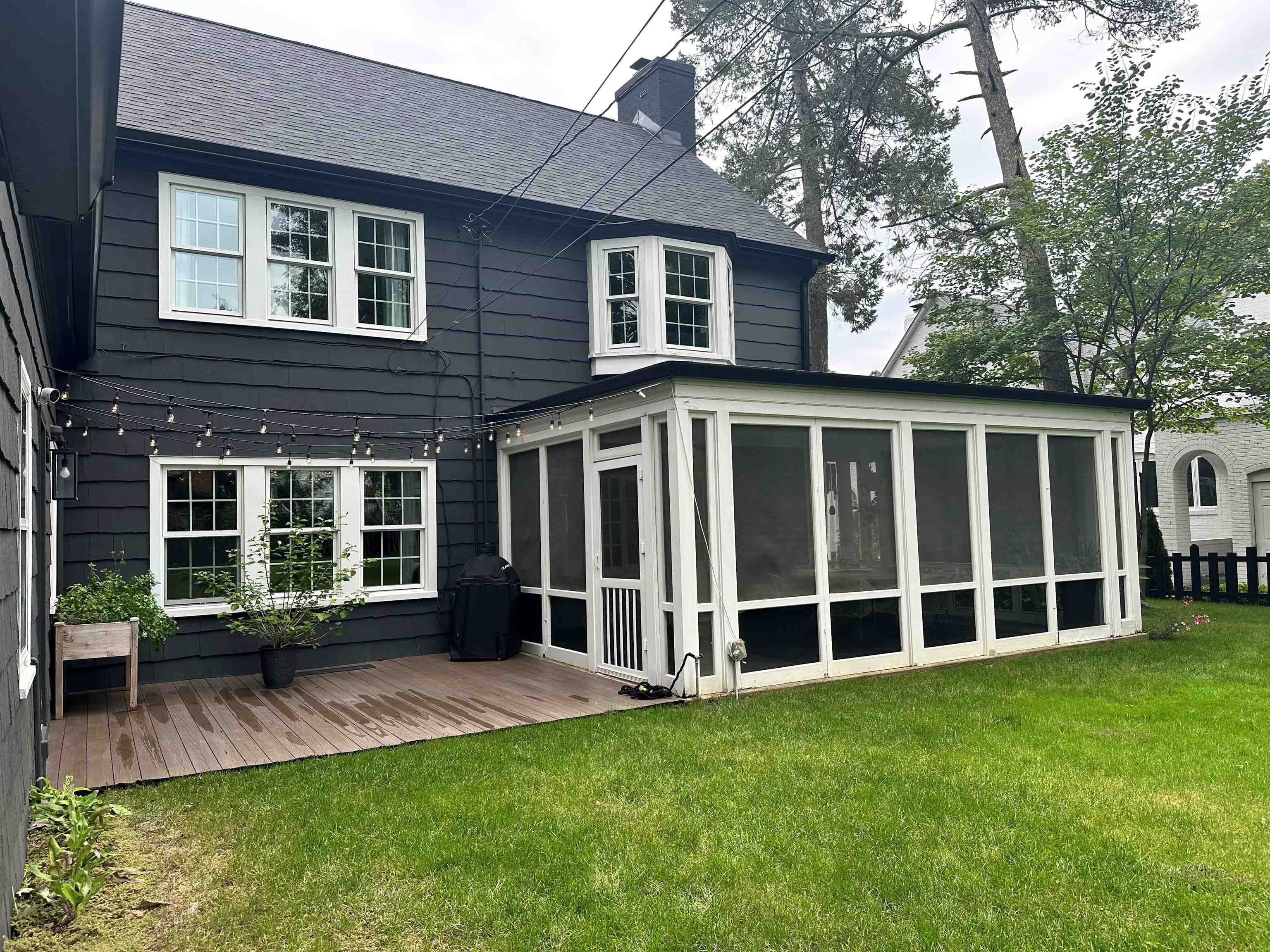 Rear of a dark two-story house with a white-framed sunroom, deck, and lawn.