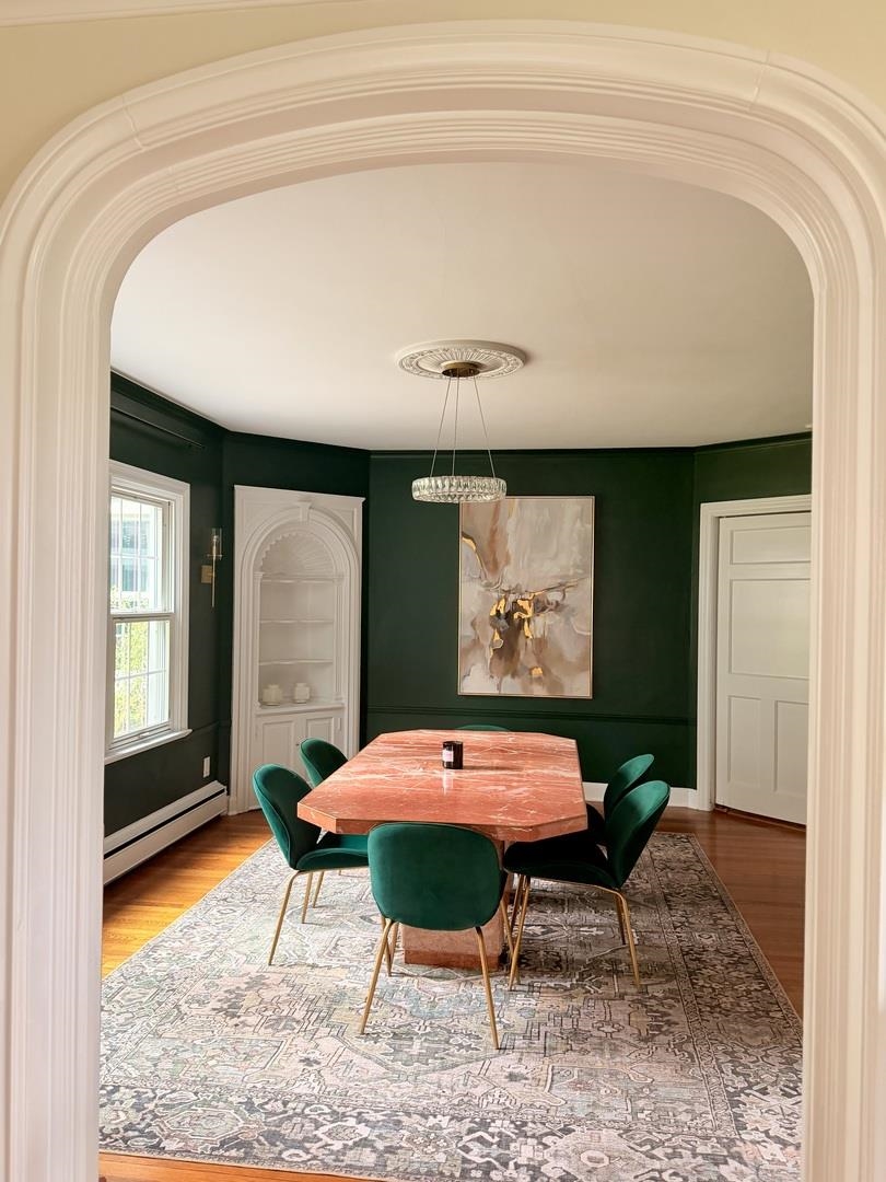 Dining room with a pink stone table, green velvet chairs, and deep green walls.