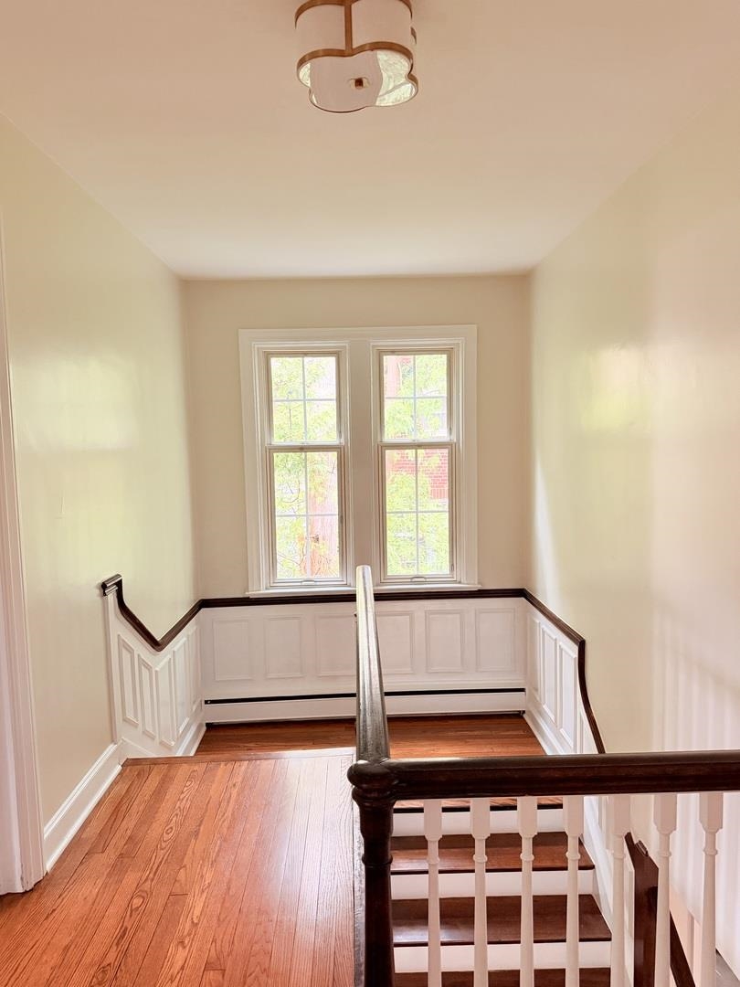 Stair landing with tall windows, polished hardwood floors, white wainscoting, and dark wood railing.