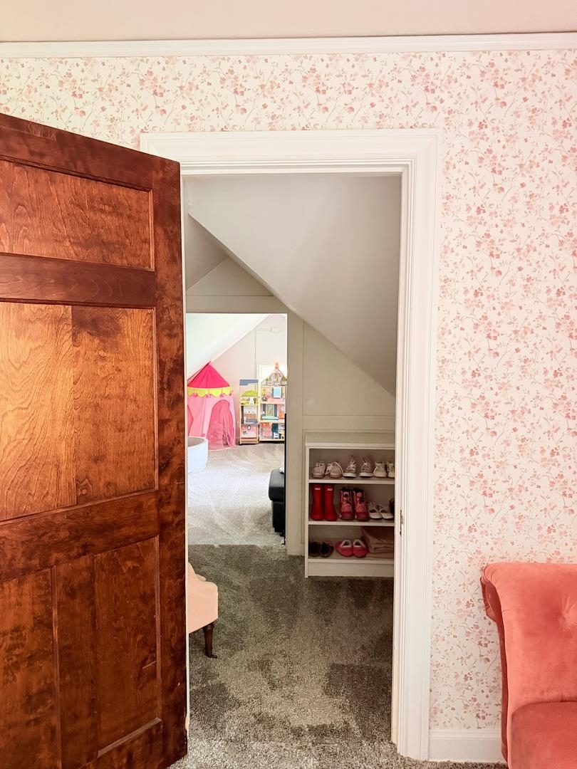 Open wooden doorway reveals a carpeted room with a sloped ceiling and shoe shelves.