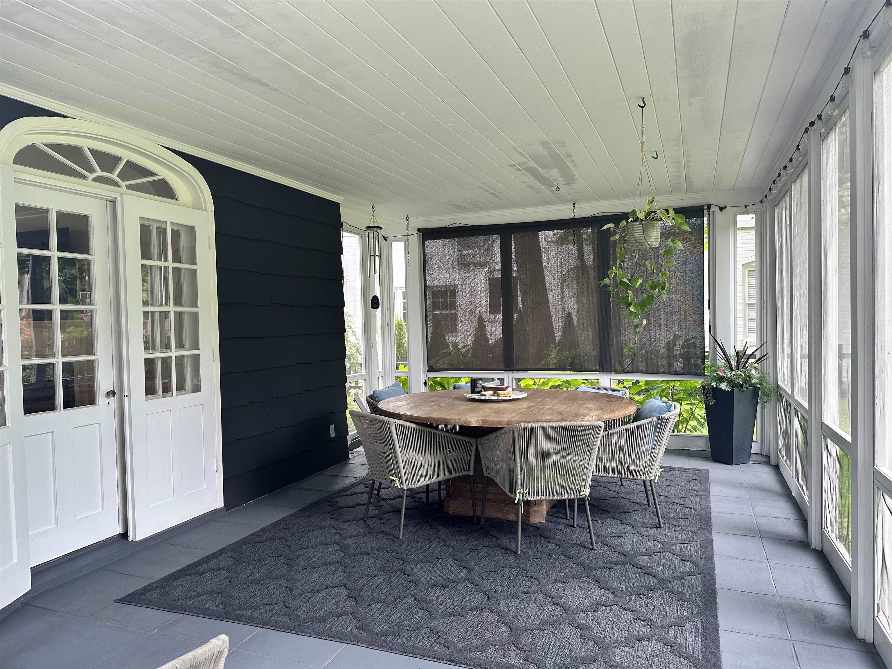 Screened porch with a round wooden dining table, woven chairs, and hanging greenery.