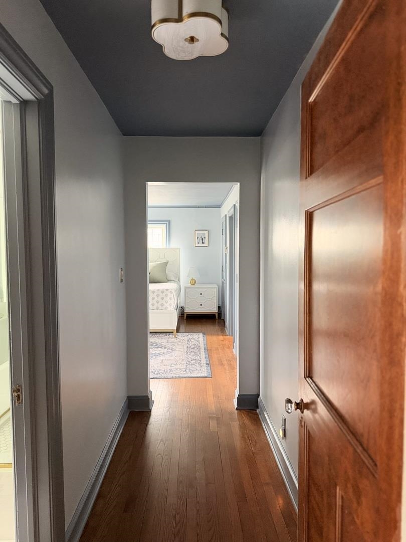 Hallway with hardwood floors and a paneled wooden door leading to a furnished bedroom.