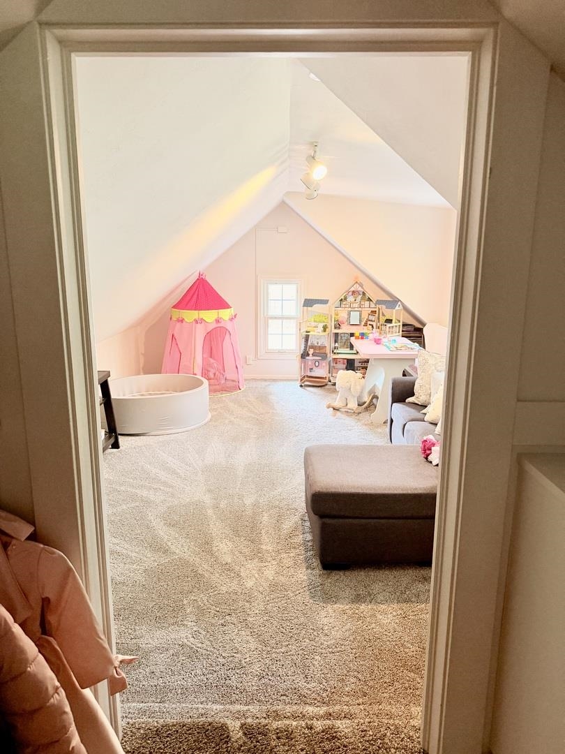 Attic playroom with a pink play tent, dollhouse, and children's table beneath a sloped ceiling.