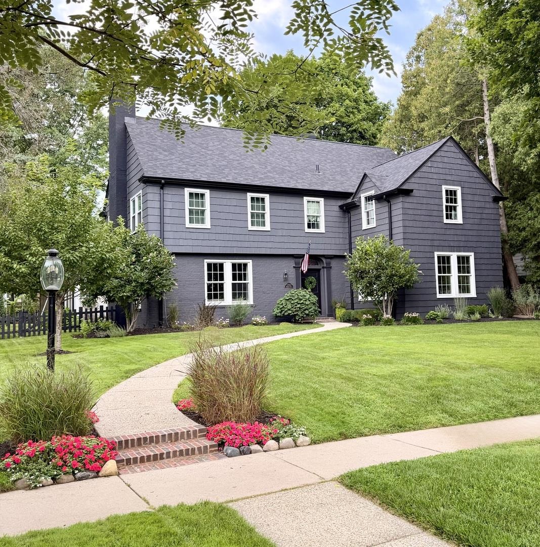 Dark gray two-story house with white-trimmed windows, a curved front walkway, and flower beds.