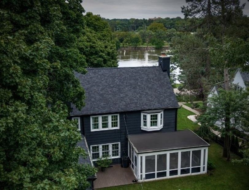Aerial view of a dark two-story home with a screened porch beside a river.