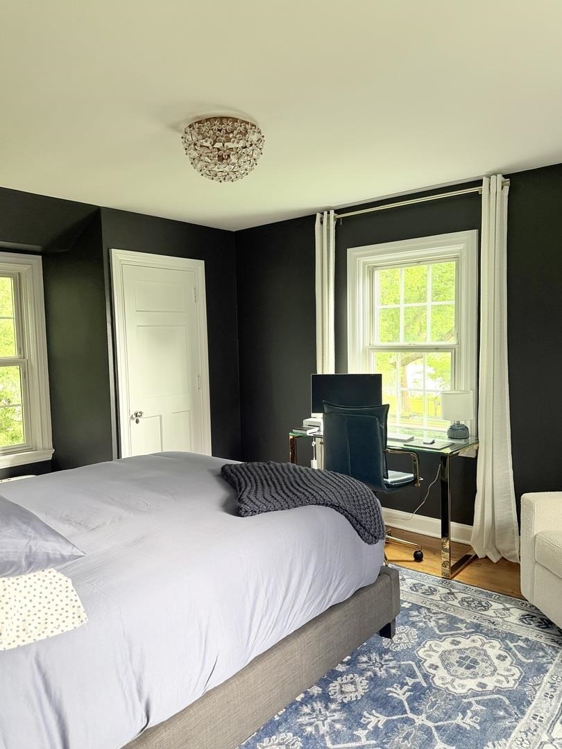 Bedroom with dark walls, a large bed, and a desk beside a bright window.