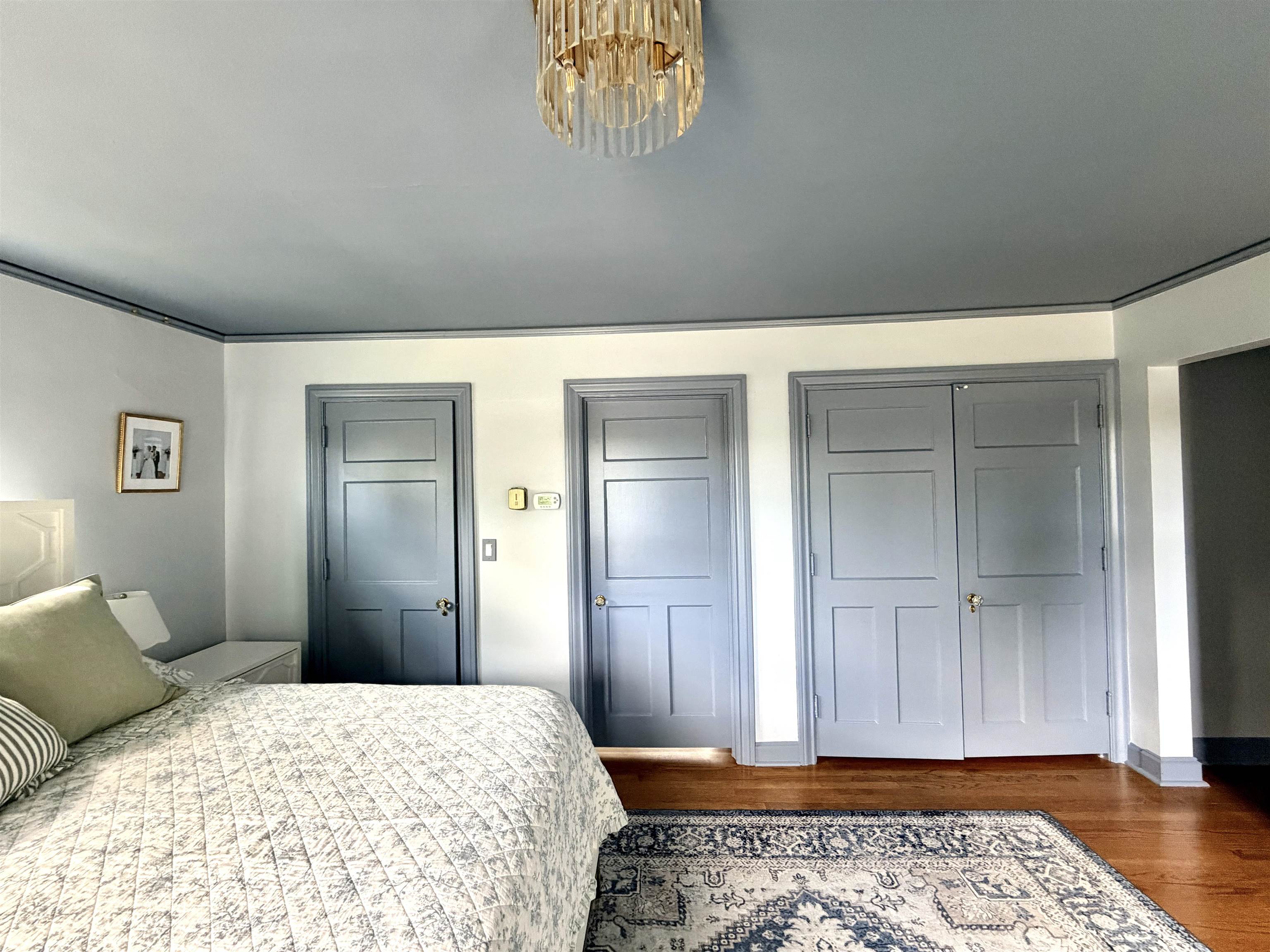 Bedroom with a patterned bed and rug, gray paneled doors, and hardwood floors.
