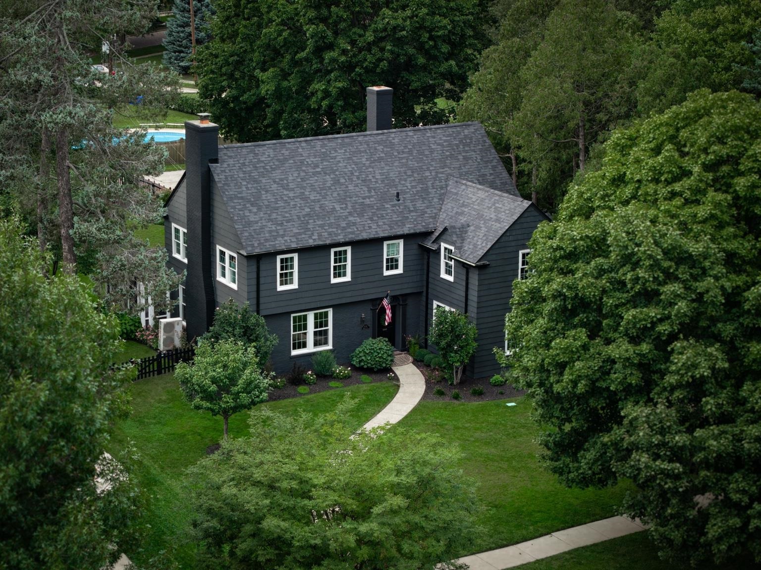 Dark charcoal two-story house with a steep gray roof, curved front walk, and mature trees.