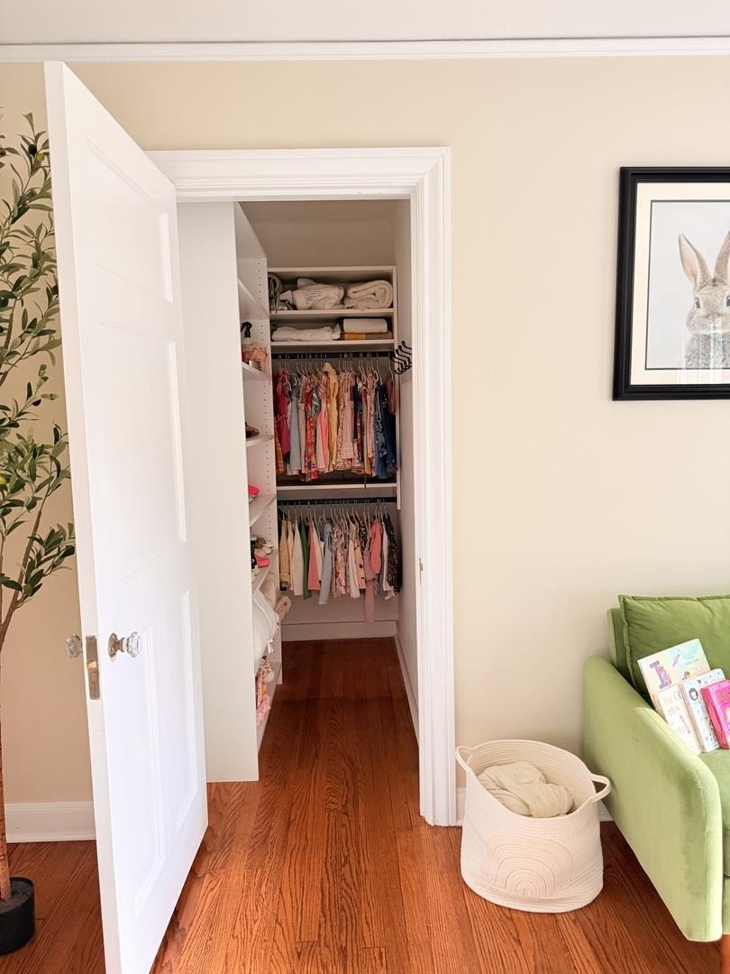 Walk-in closet with two rows of hanging clothes, open shelving, and hardwood flooring.