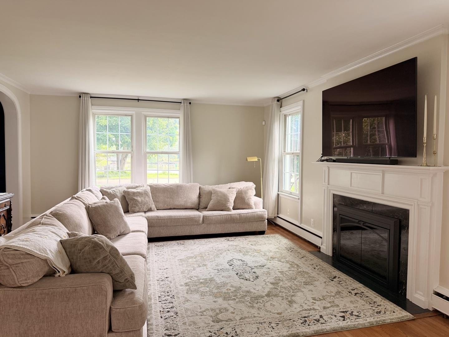 Living room with a beige sectional, patterned rug, white fireplace, and large windows.