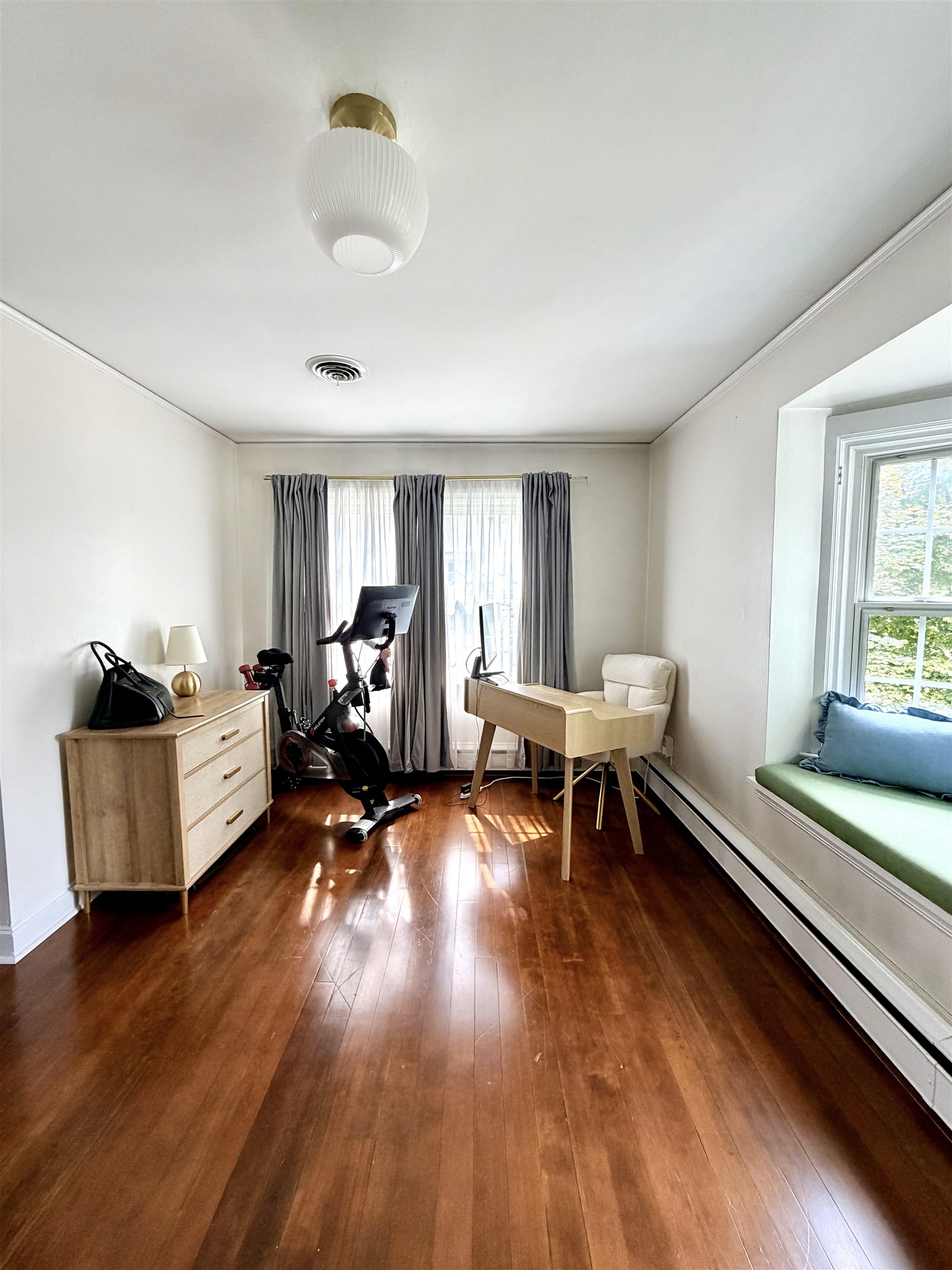 Home office with a stationary exercise bike, hardwood floors, and a window seat.