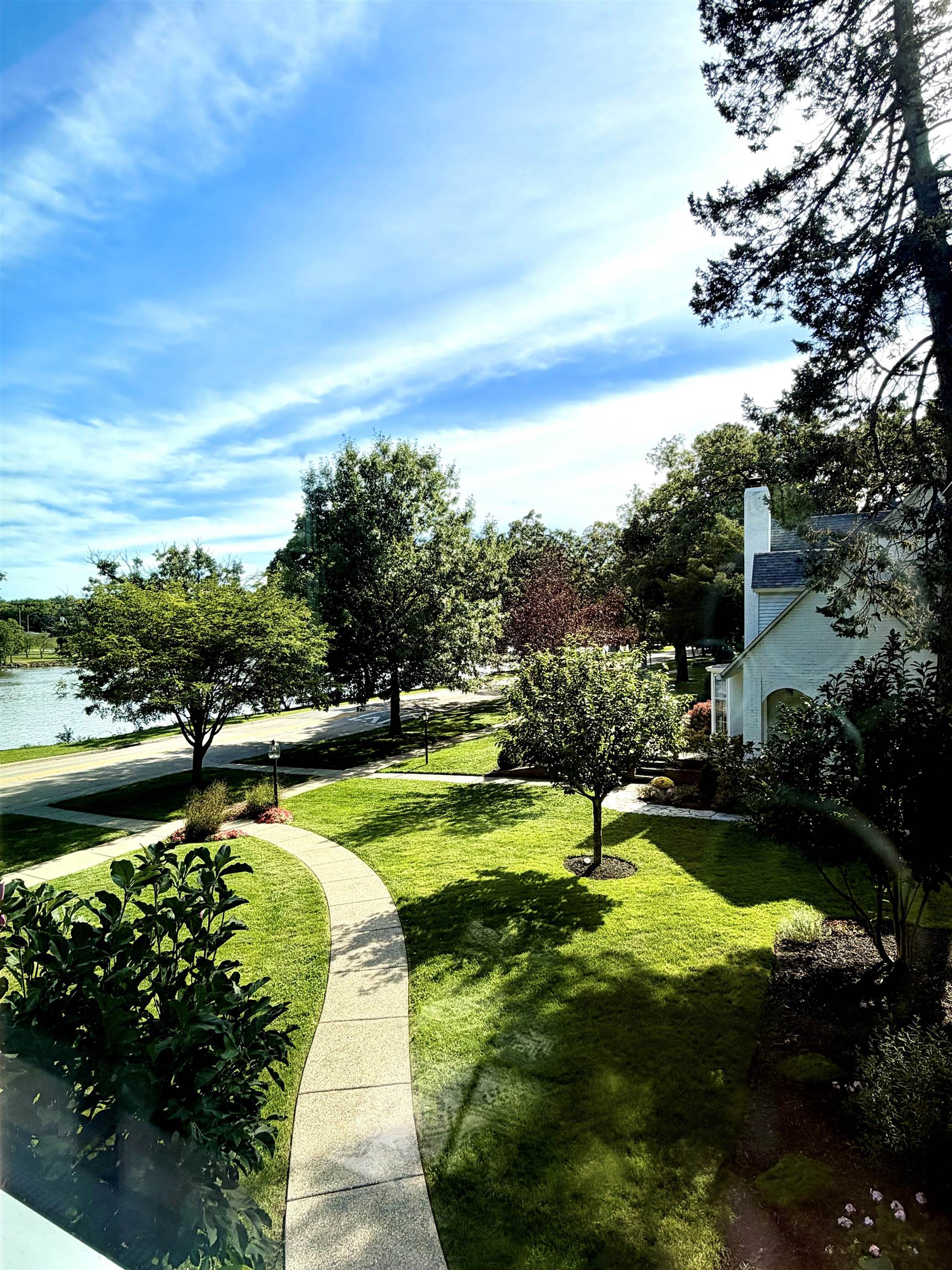 White house beside a landscaped lawn and curved walkway, with water visible across the road.