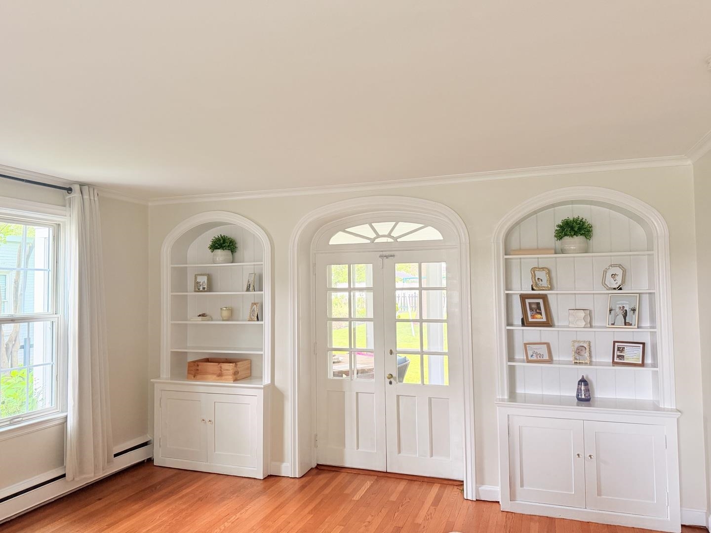 Bright room with arched built-in shelves, hardwood floors, and glass-paneled double doors.