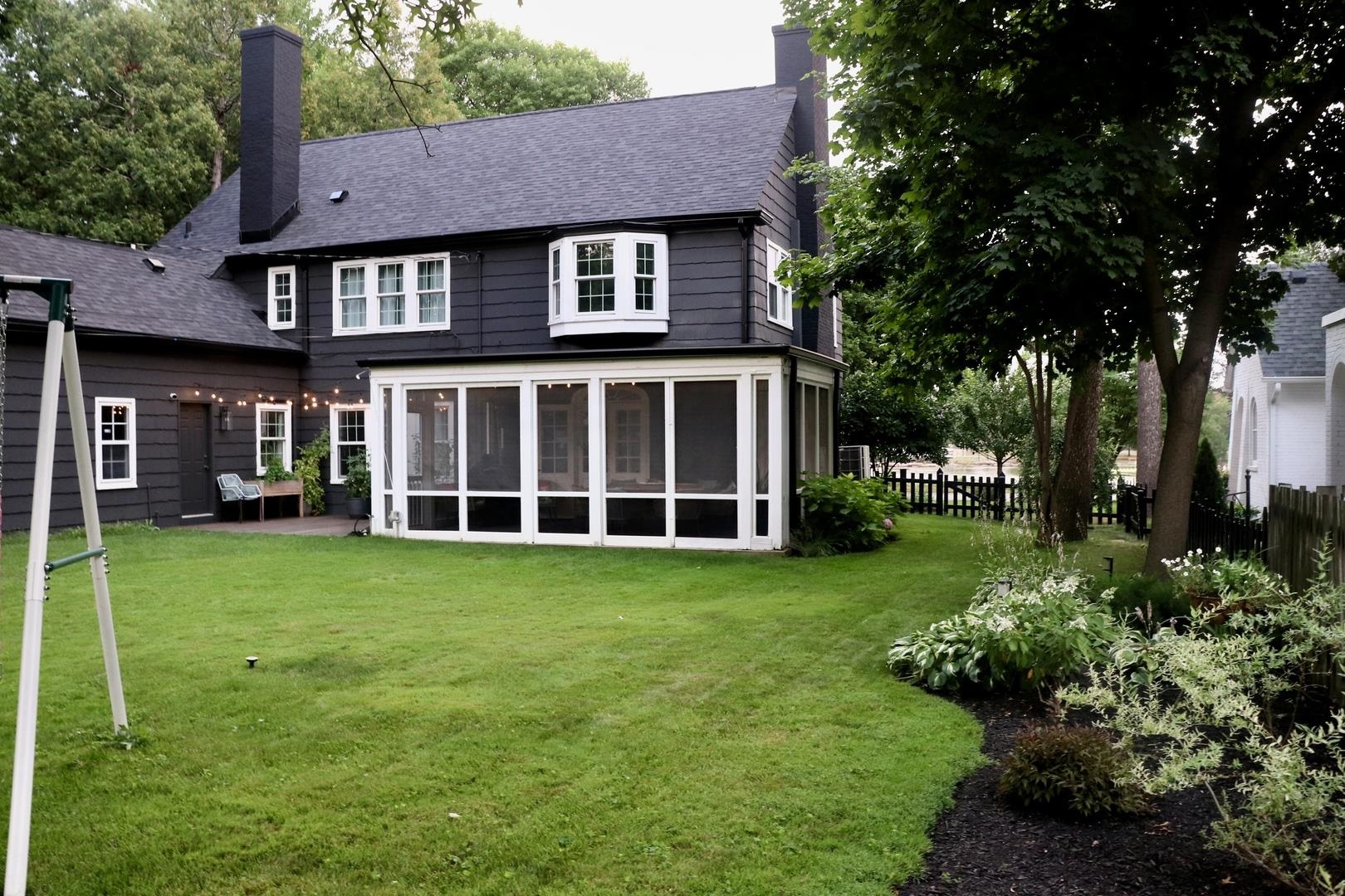 Rear of a dark gray house with a screened porch overlooking a leafy backyard lawn.