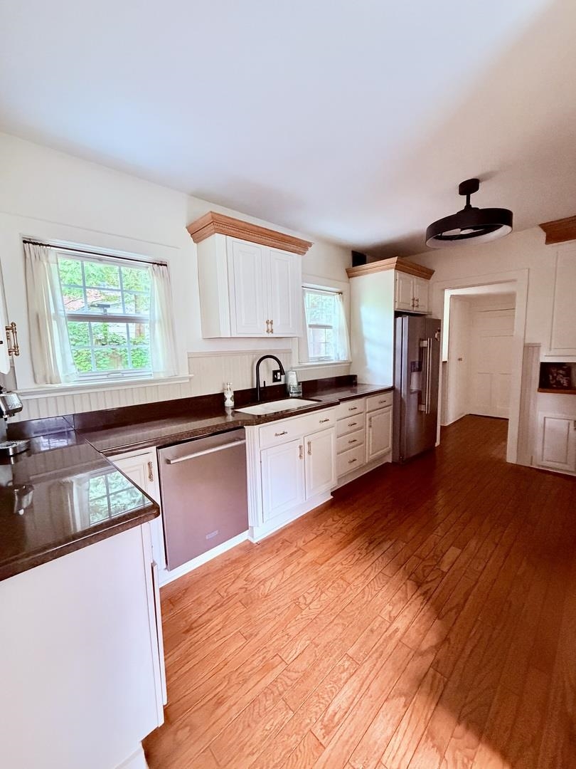 Kitchen with white cabinetry, dark countertops, stainless appliances, and warm hardwood floors.